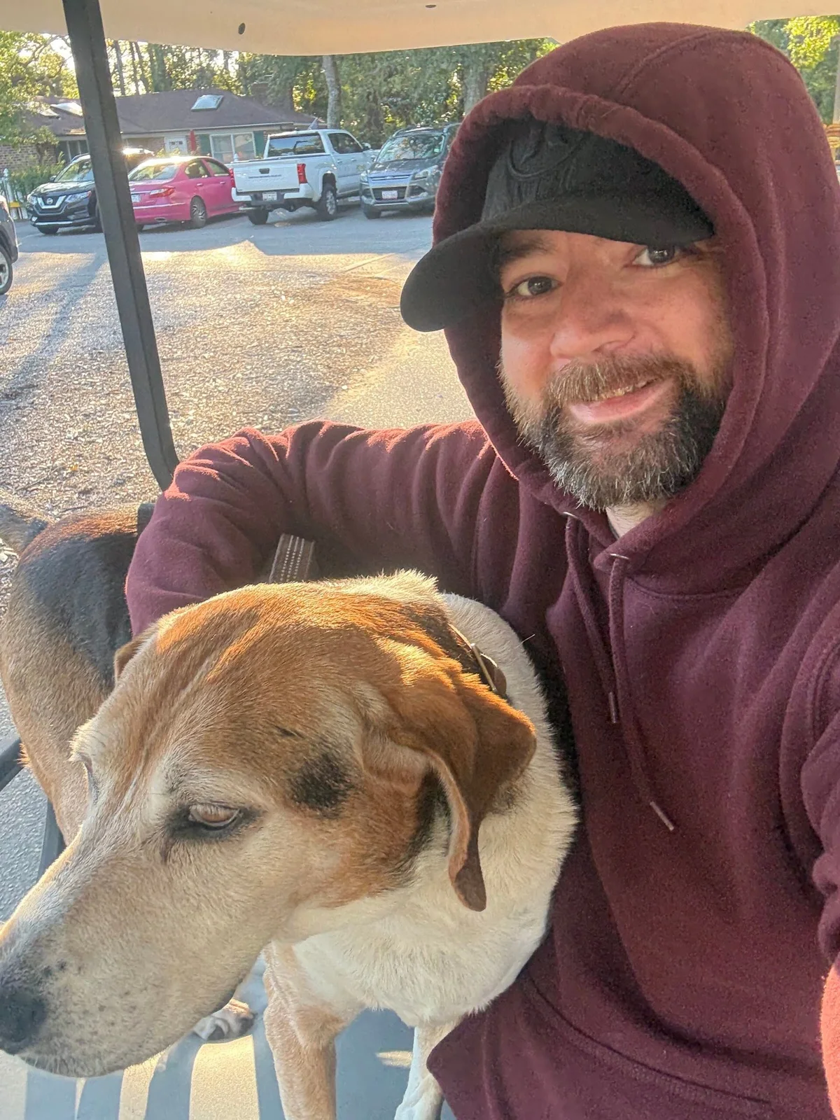 Jason in a burgundy hoodie sitting beside the family hound under a golf-cart roof