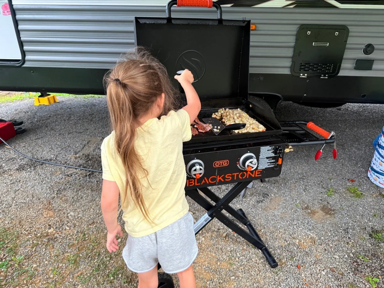 Our daughter helping cook bacon and breakfast potatoes on the Blackstone at the campsite